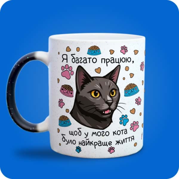 Біла чашка з чорним котом, лапками, кормом і написом "Я багато працюю, щоб у мого кота було найкраще життя", вигляд з лівого боку
