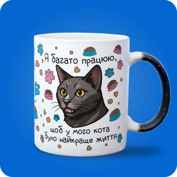 Біла чашка з чорним котом, лапками, кормом і написом "Я багато працюю, щоб у мого кота було найкраще життя", вигляд з правого боку