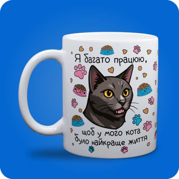 Біла чашка з чорним котом, лапками, кормом і написом "Я багато працюю, щоб у мого кота було найкраще життя", вигляд чашки біла з блискітками і без блискіток