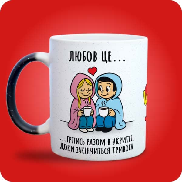 Біла чашка в стилі Love is із закоханою парою під ковдрою та написом "Грітись разом в укритті, доки закінчиться тривога", вигляд з лівого боку